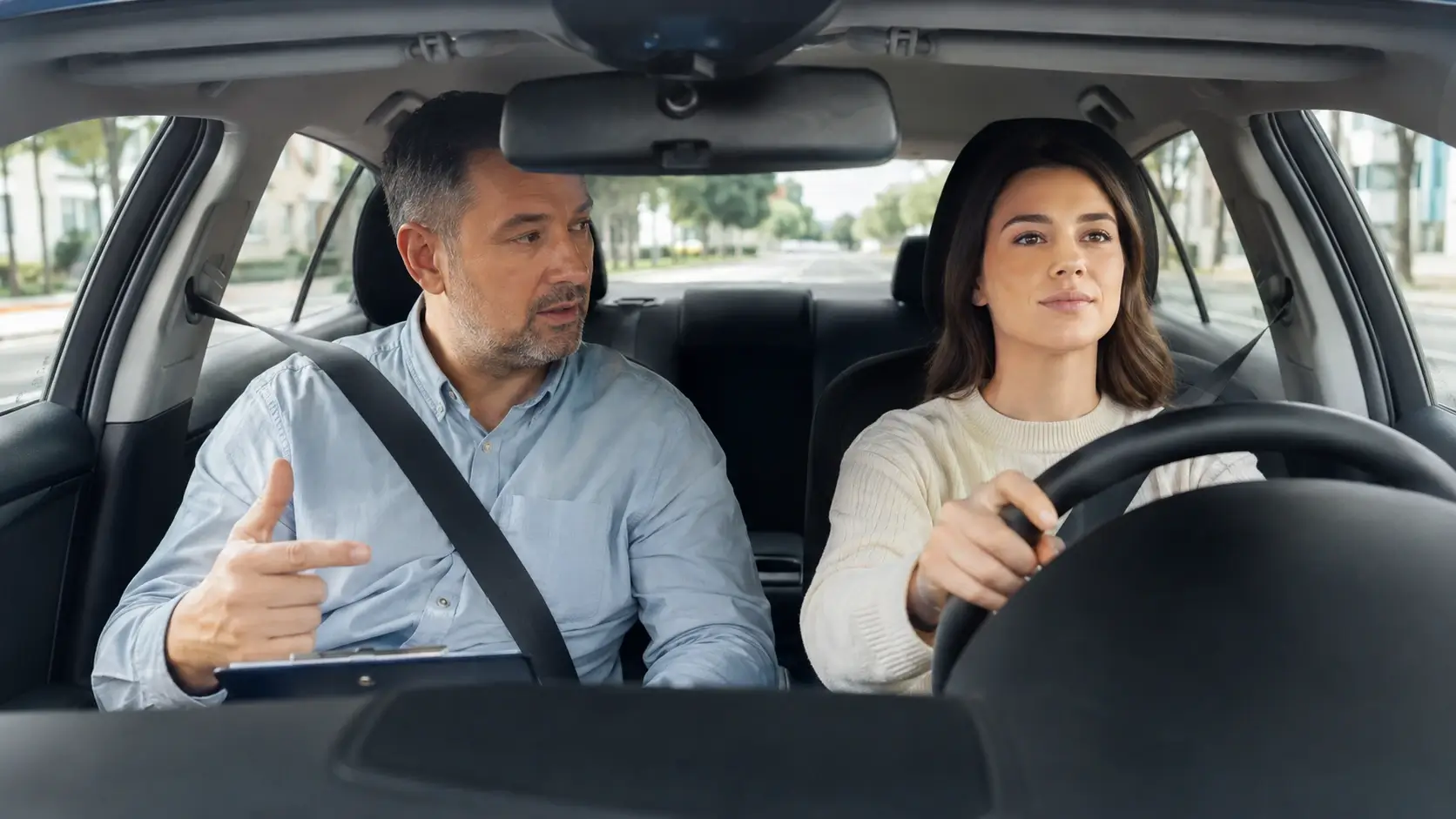 Driving instructor coaching an adult learner behind the wheel during a practical driving lesson in a training car.