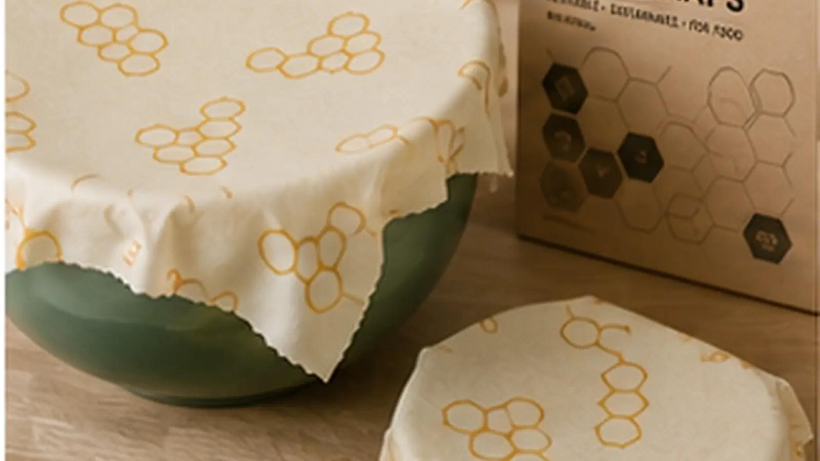 Realistic beeswax reusable food wraps hero image showing eco-friendly patterned wraps covering bowls and food on a natural wooden kitchen surface.