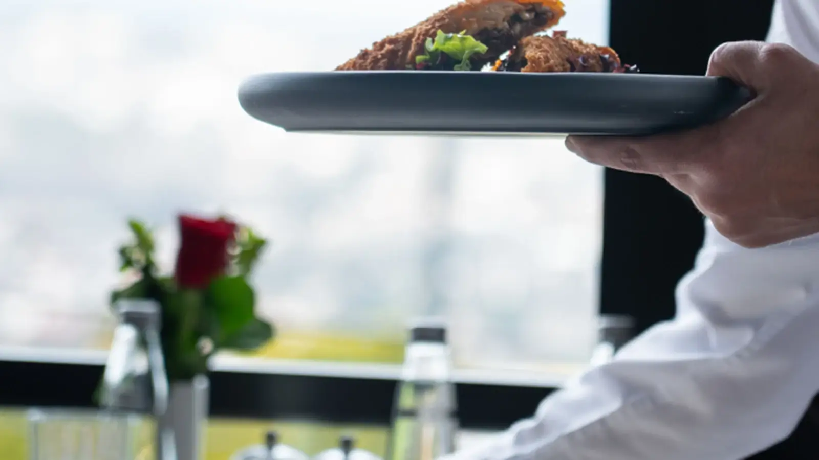 A waiter serving a plated dish in a restaurant dining setting, representing food and hospitality services.