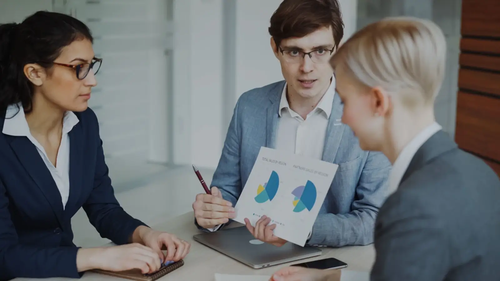 Business professionals reviewing charts and discussing sales strategy in an office meeting.