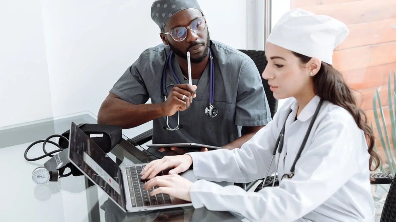 Two healthcare professionals working together on a laptop during a medical consultation and planning session.