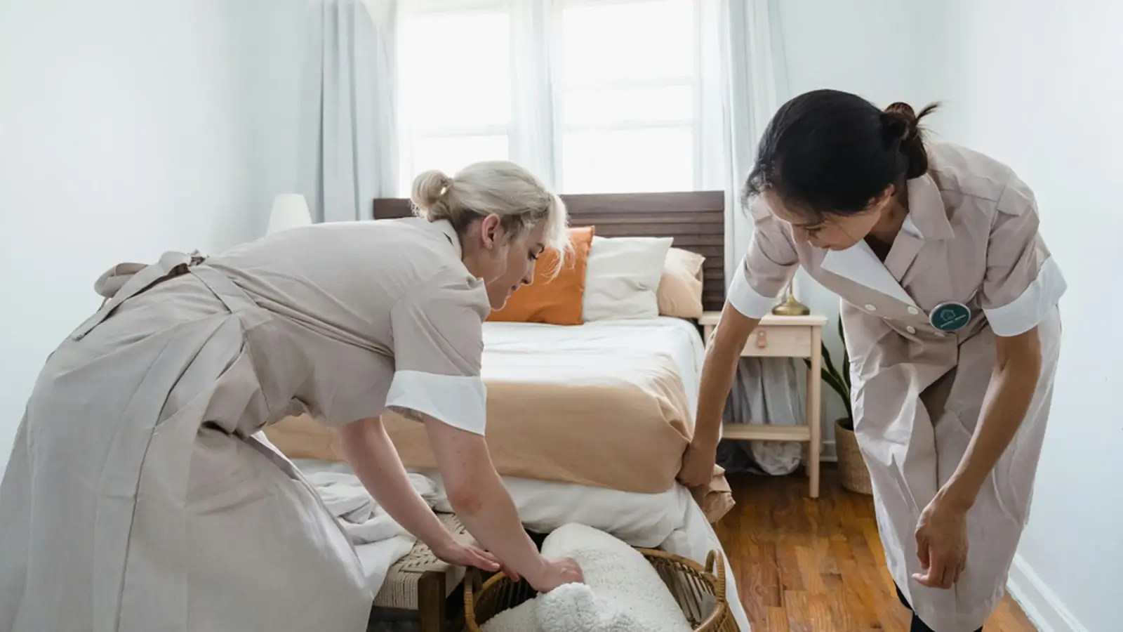 Home service staff making a bed in a clean bedroom, representing personal care and home services.